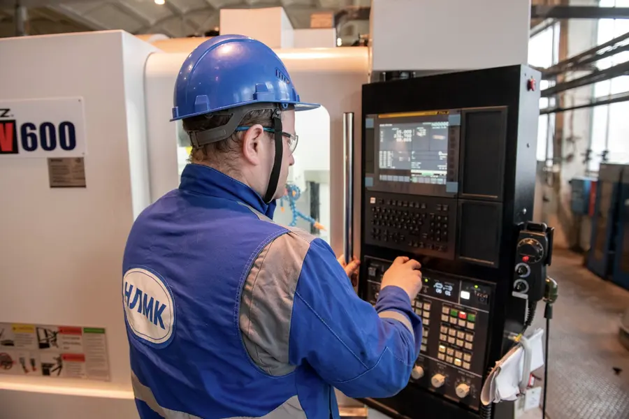 Un opérateur en bleu de travail, casque sur la tête, se tient debout devant le pupitre de commande de sa machine.